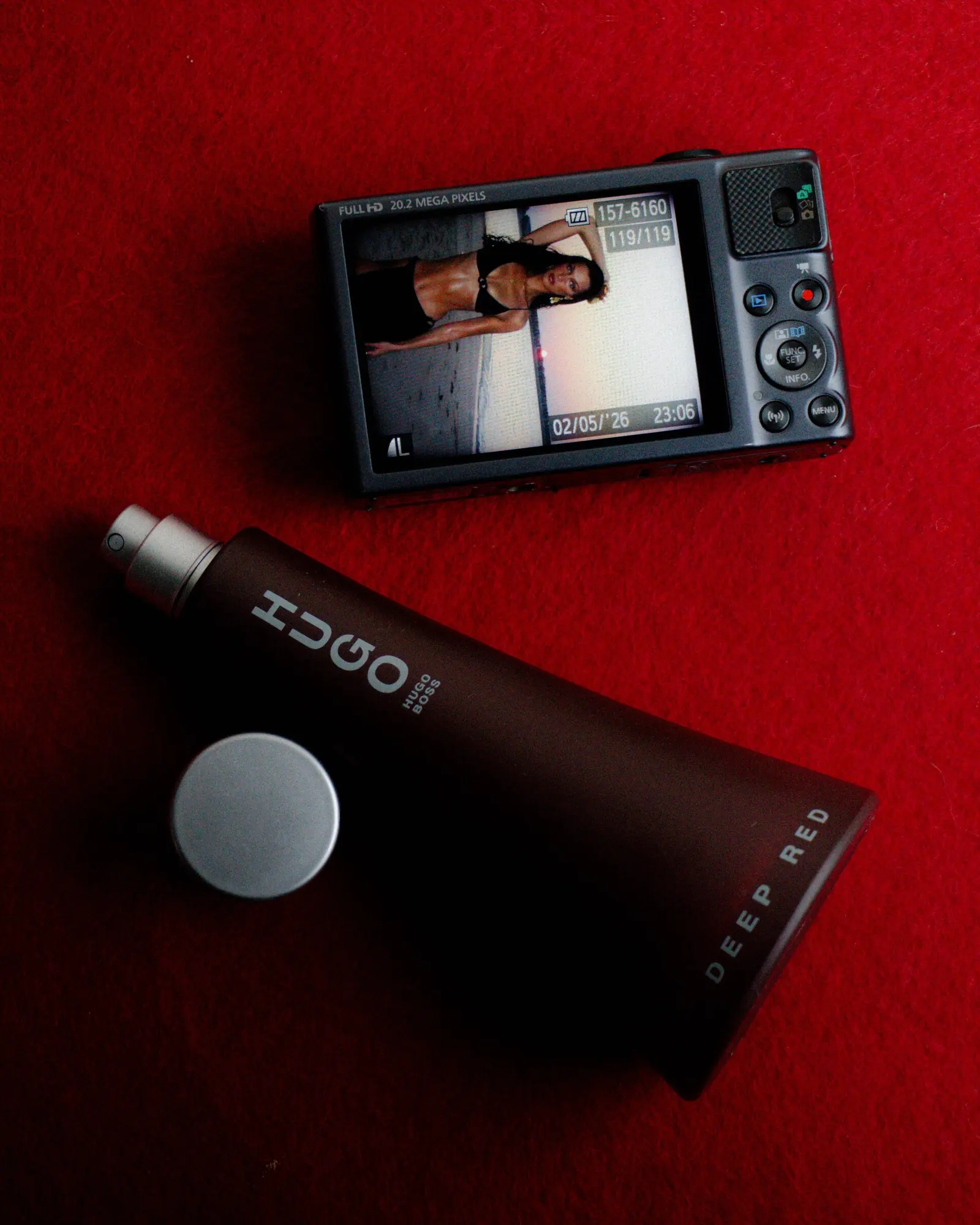 The back screen of a Canon compact next to a Hugo Deep Red bottle on red felt