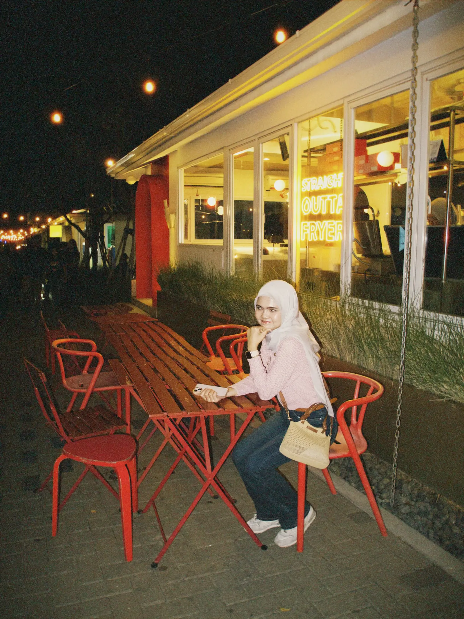 A girl at a red table outside a glowing cafe at night
