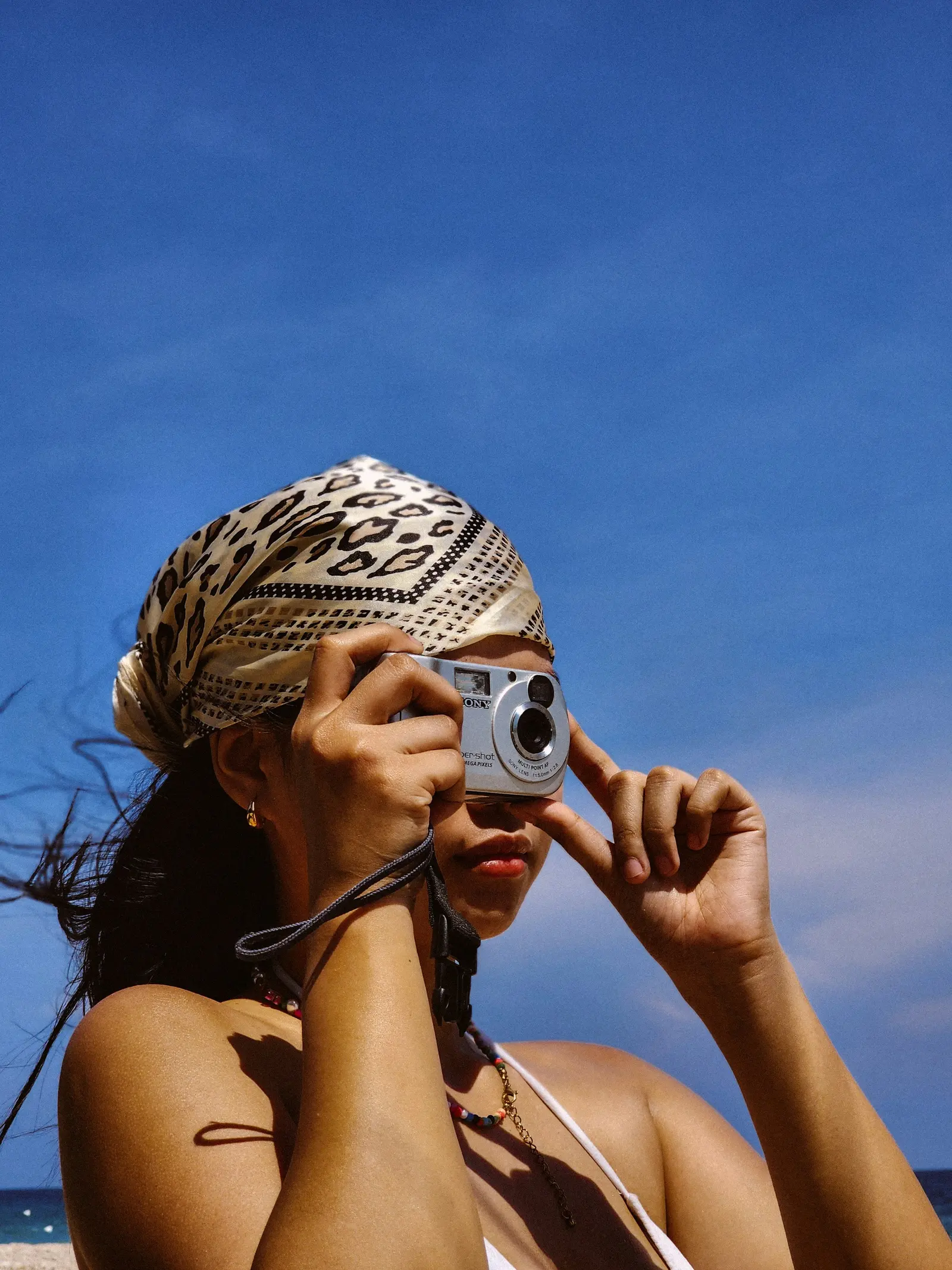A girl taking a selfie with a compact camera against a blue sky